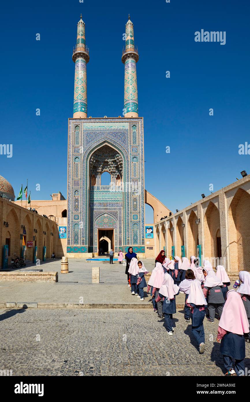 Little Iranian schoolgirls in school uniform with pink hijabs walk to the Jameh Mosque of Yazd, 14th-century Shia mosque in the Old Town of Yazd, Iran Stock Photo
