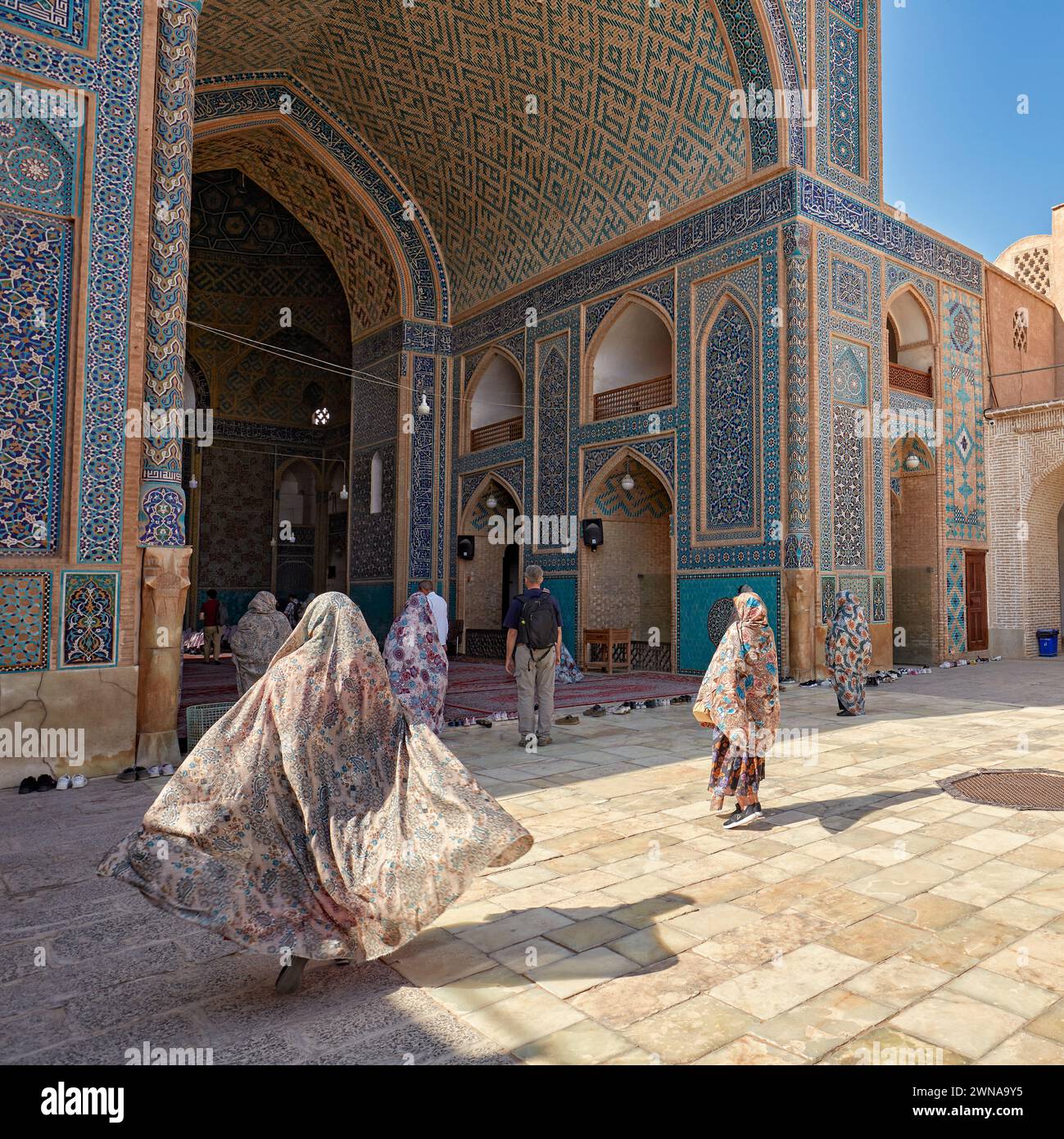 Woman with her chador flowing in the wind walks to the entrance of the Jameh Mosque of Yazd, 14th-century Shia mosque in the Old Town of Yazd, Iran. Stock Photo