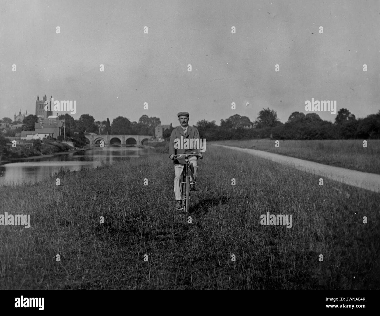 1901 Historic Black and White Photograph of Cyclist on Bishops Meadow by River Wye, and Wye Bridge & Cathedral, Hereford, Herefordshire, England, UK Stock Photo
