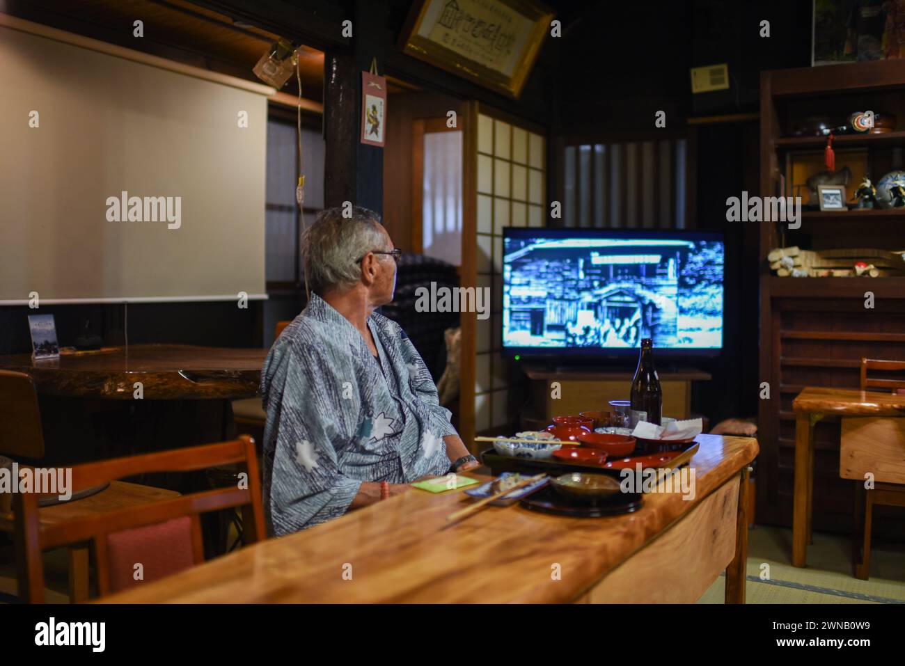 Guest watching television at dinner in Gassho Minshuku Nakaya Ryuokan in UNESCO World Heritage Gassho-zukuri Village of Ainokura, Japan Stock Photo