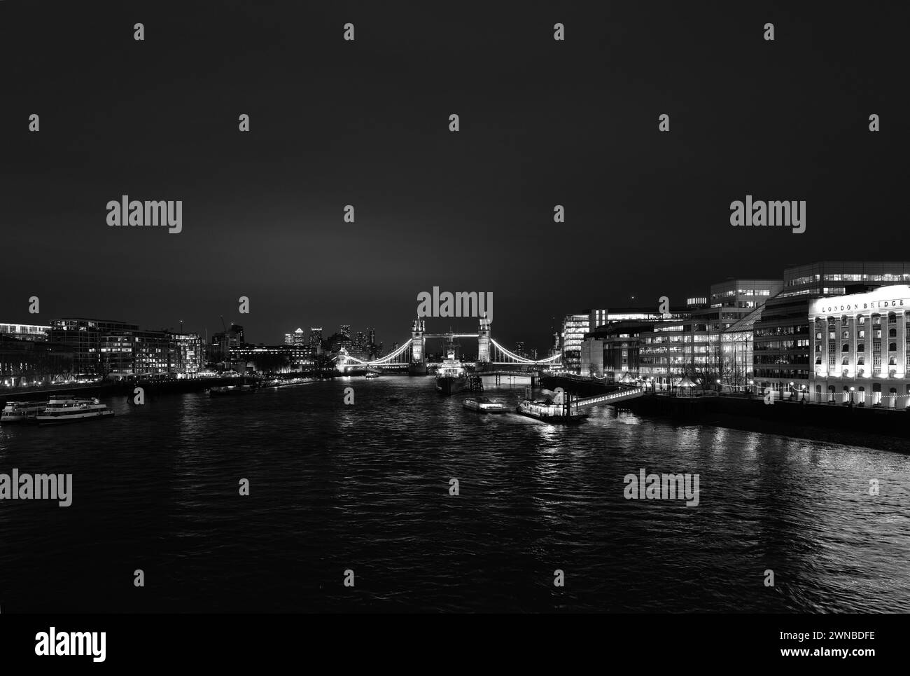 Powerful abstract monochrome architectural illuminated night landscape of The River Thames shot from London Bridge and showing Tower Bridge, Canary Wharf, Tooley Street, London Bridge Hospital, HMS Belfast, London Bridge City Pier and River Boats Stock Photo