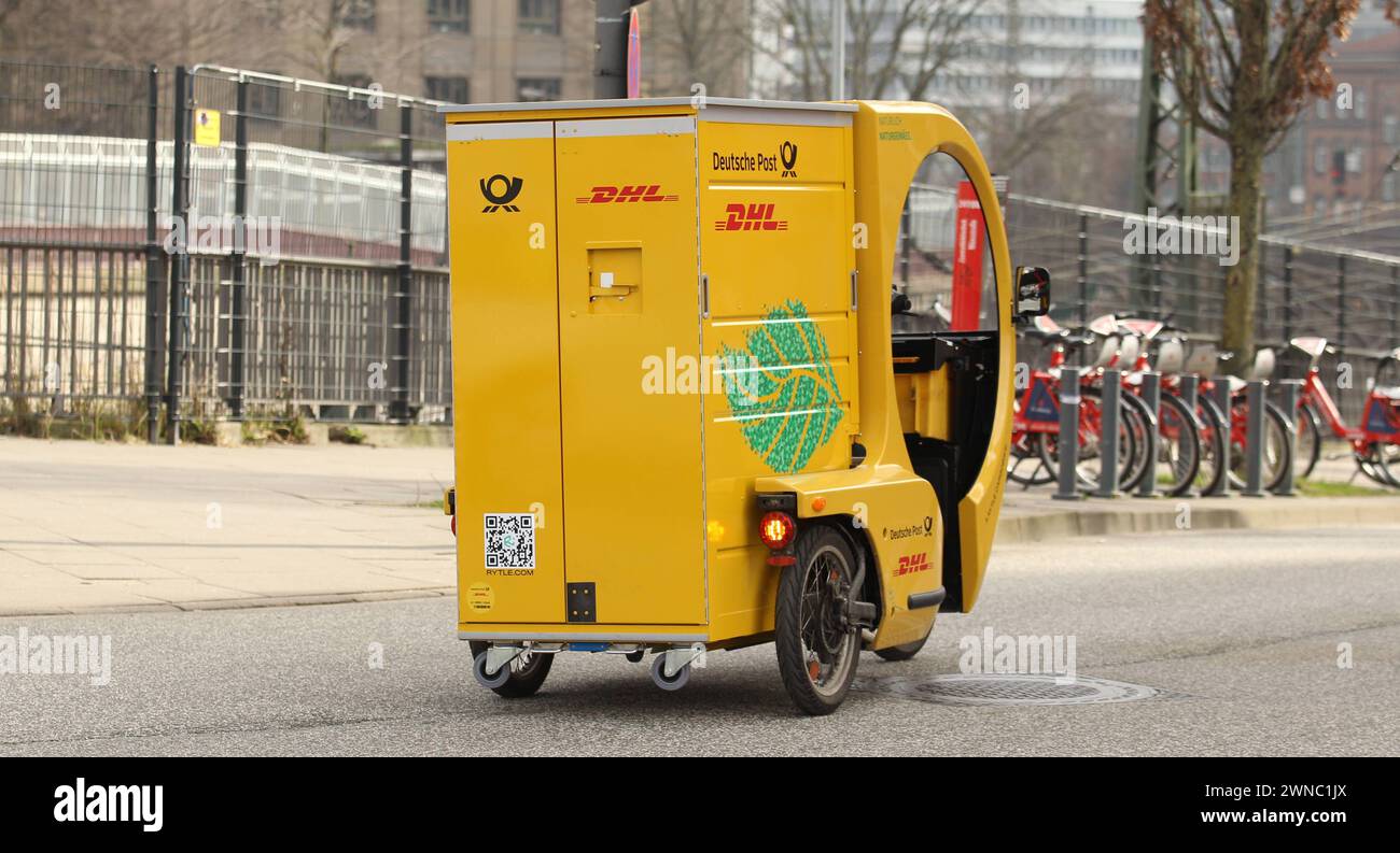 Ein Paketbote von DHL fährt mit einem Lastenrad eine Straße entlang. St. Georg Hamburg *** A DHL parcel carrier rides a cargo bike along a street in St. Georg Hamburg Stock Photo