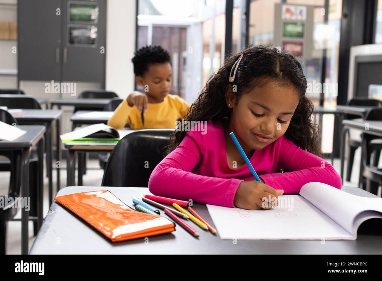 Biracial girl with curly brown hair is in a school classroom, African American boy in the background Stock Photo