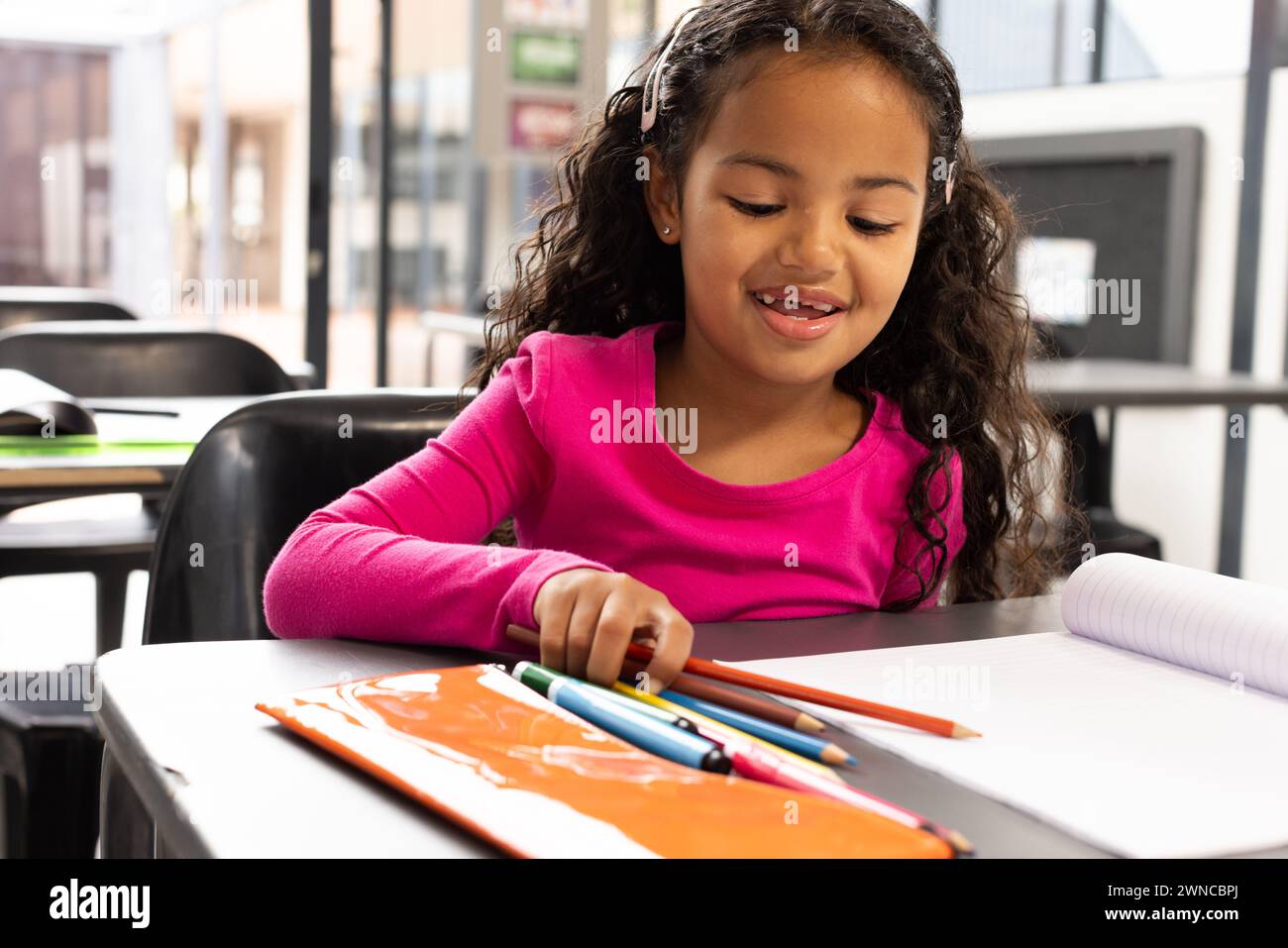 Biracial girl with curly hair draws with colored pencils in a school classroom Stock Photo