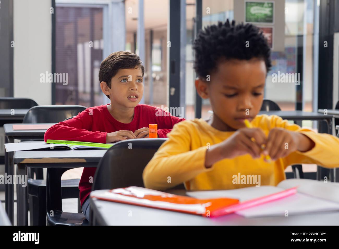 Biracial boy in red looks curious in school classroom, African American