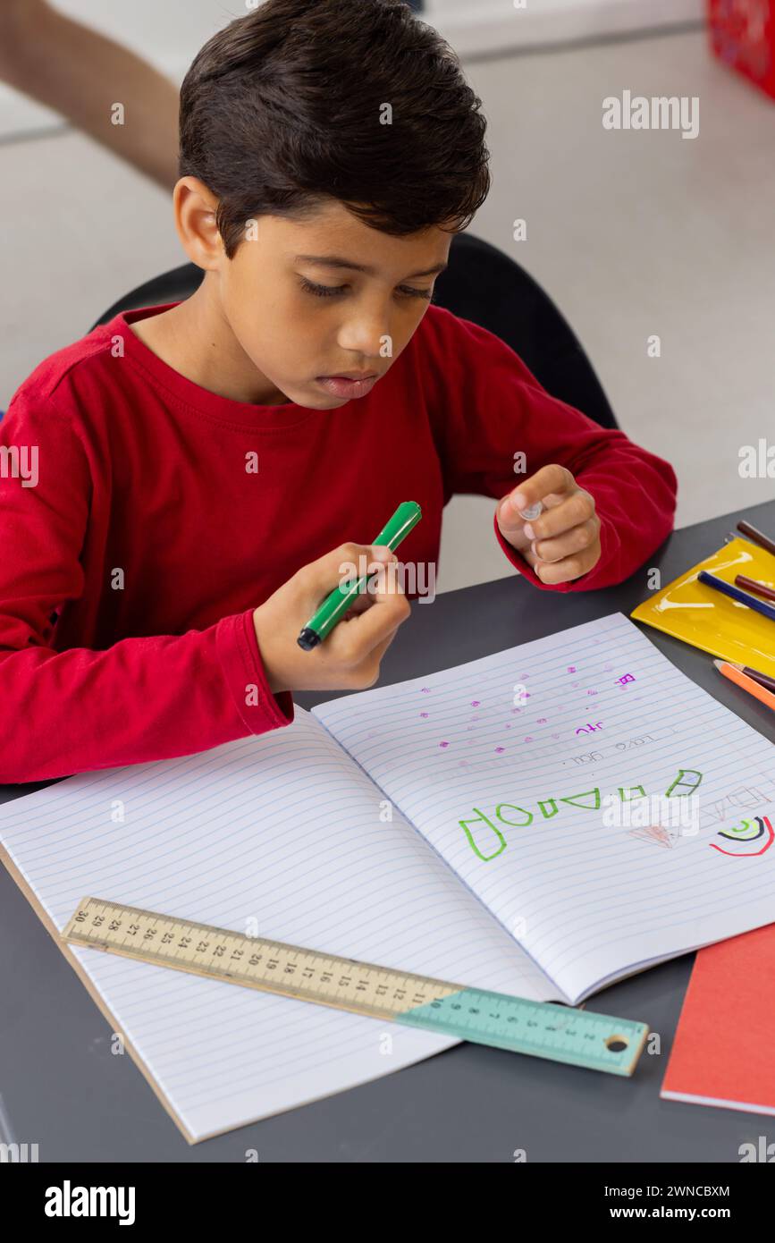 Biracial boy with dark hair is focused on writing in a notebook in a ...
