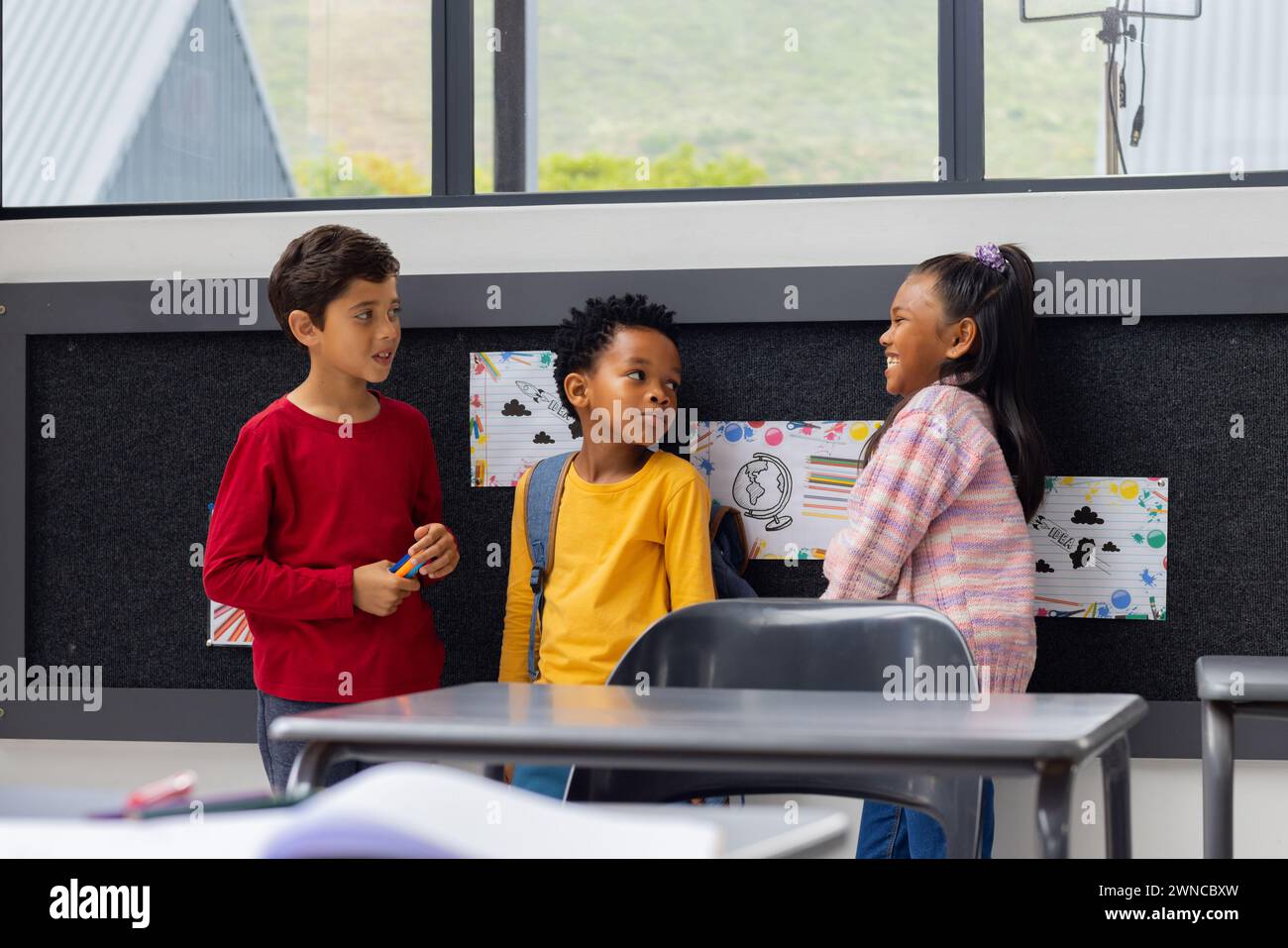 Biracial boy converses with an African American boy and biracial girl in a school classroom Stock Photo