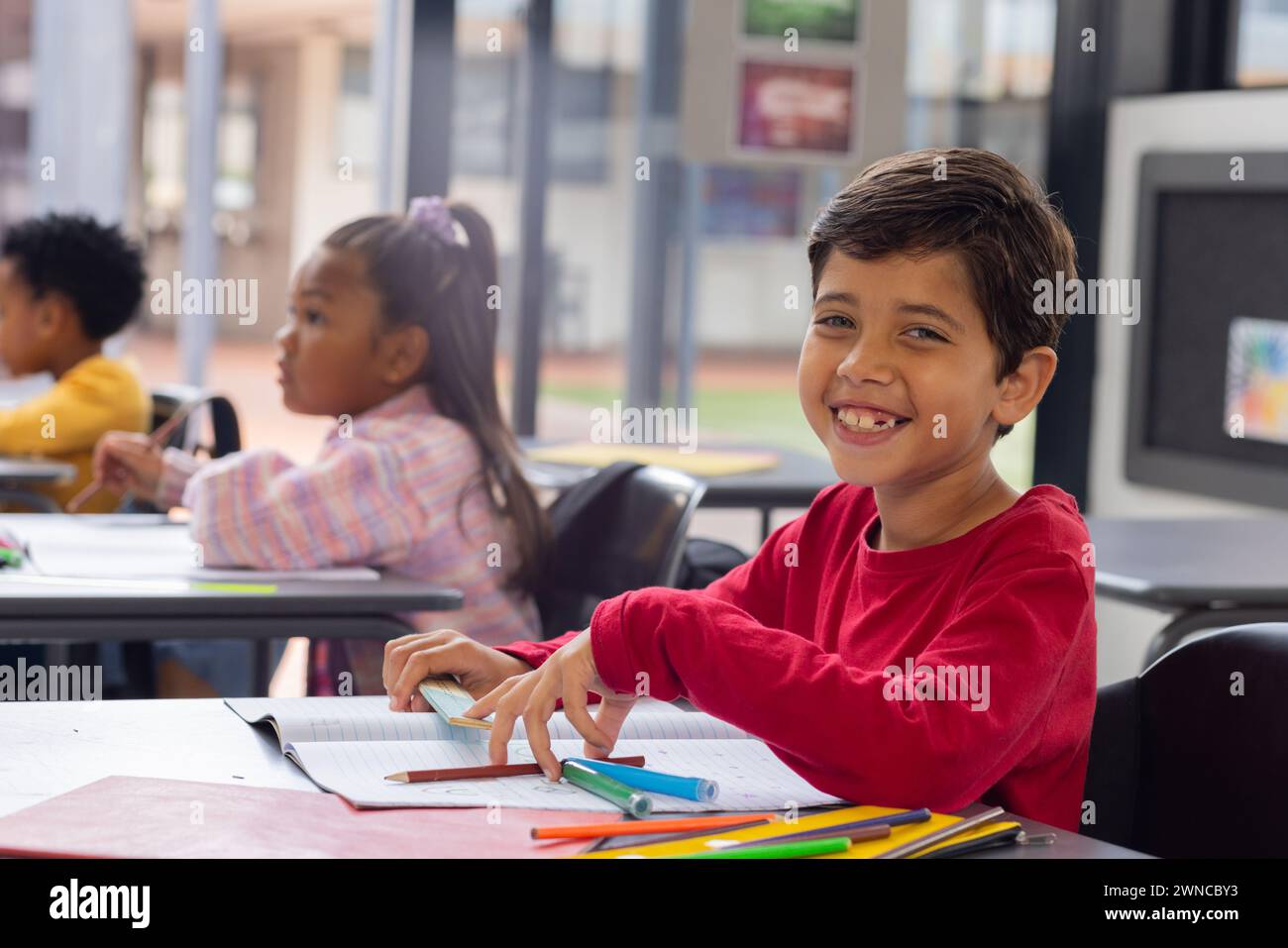 Biracial boy with a bright smile sits at a desk in a school classroom ...