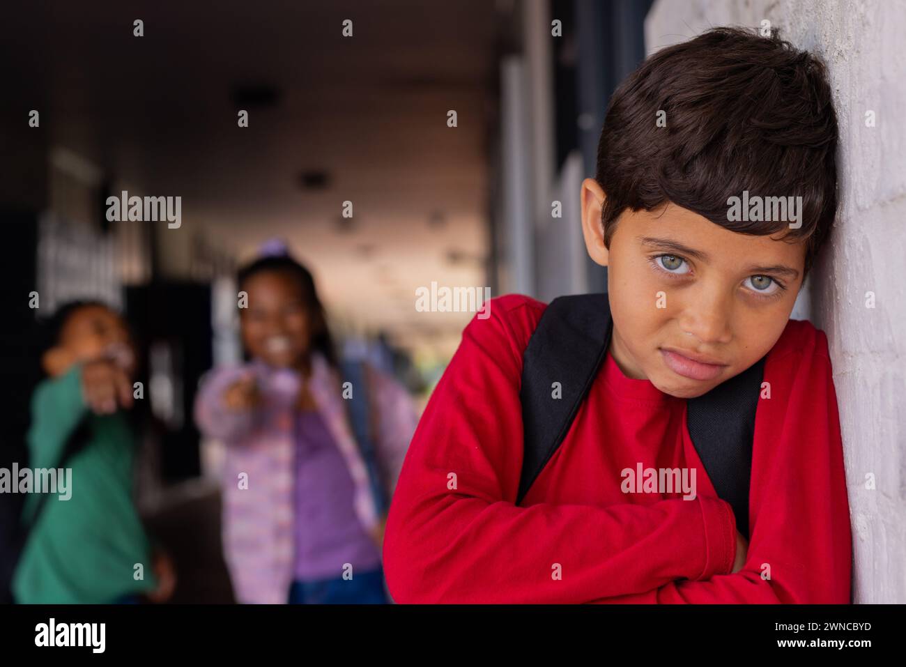 Biracial boy leans against a white wall, looking pensive, a victim of bullying in school Stock Photo