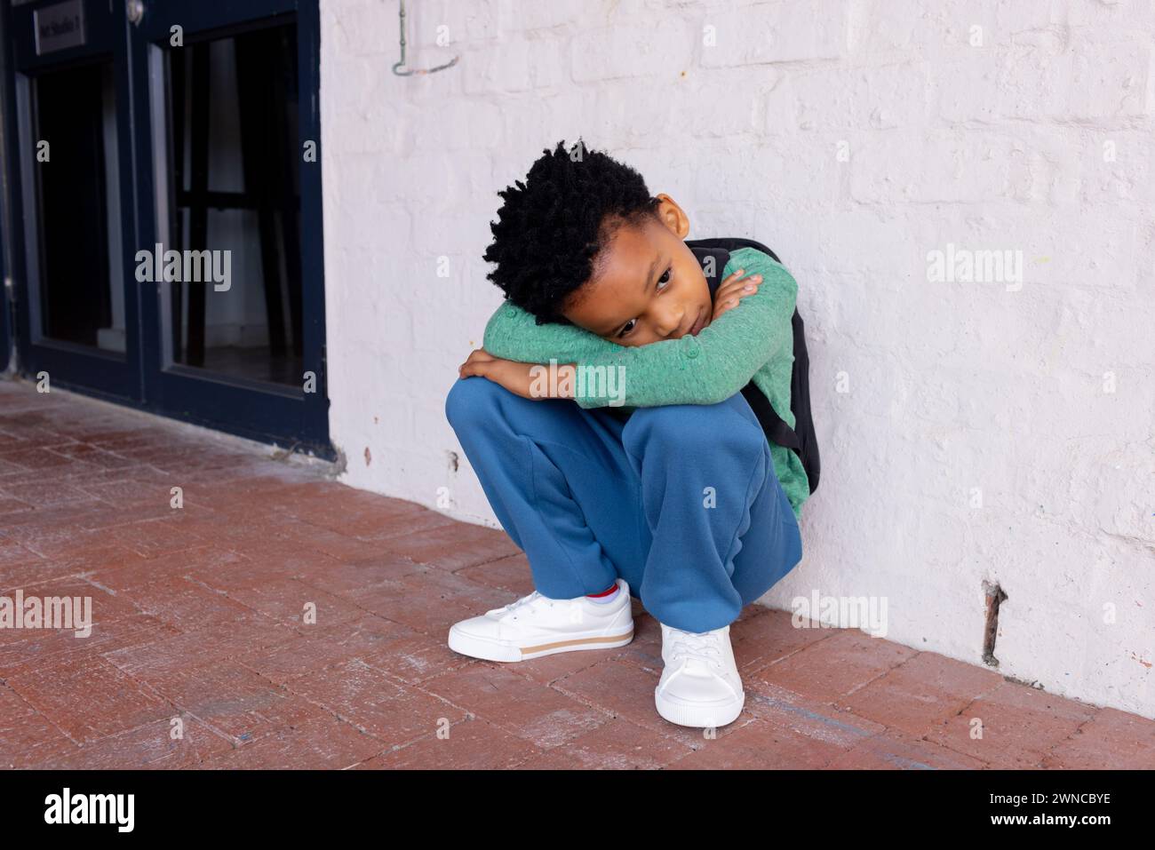 African American boy sits on the ground at school, looking sad Stock Photo