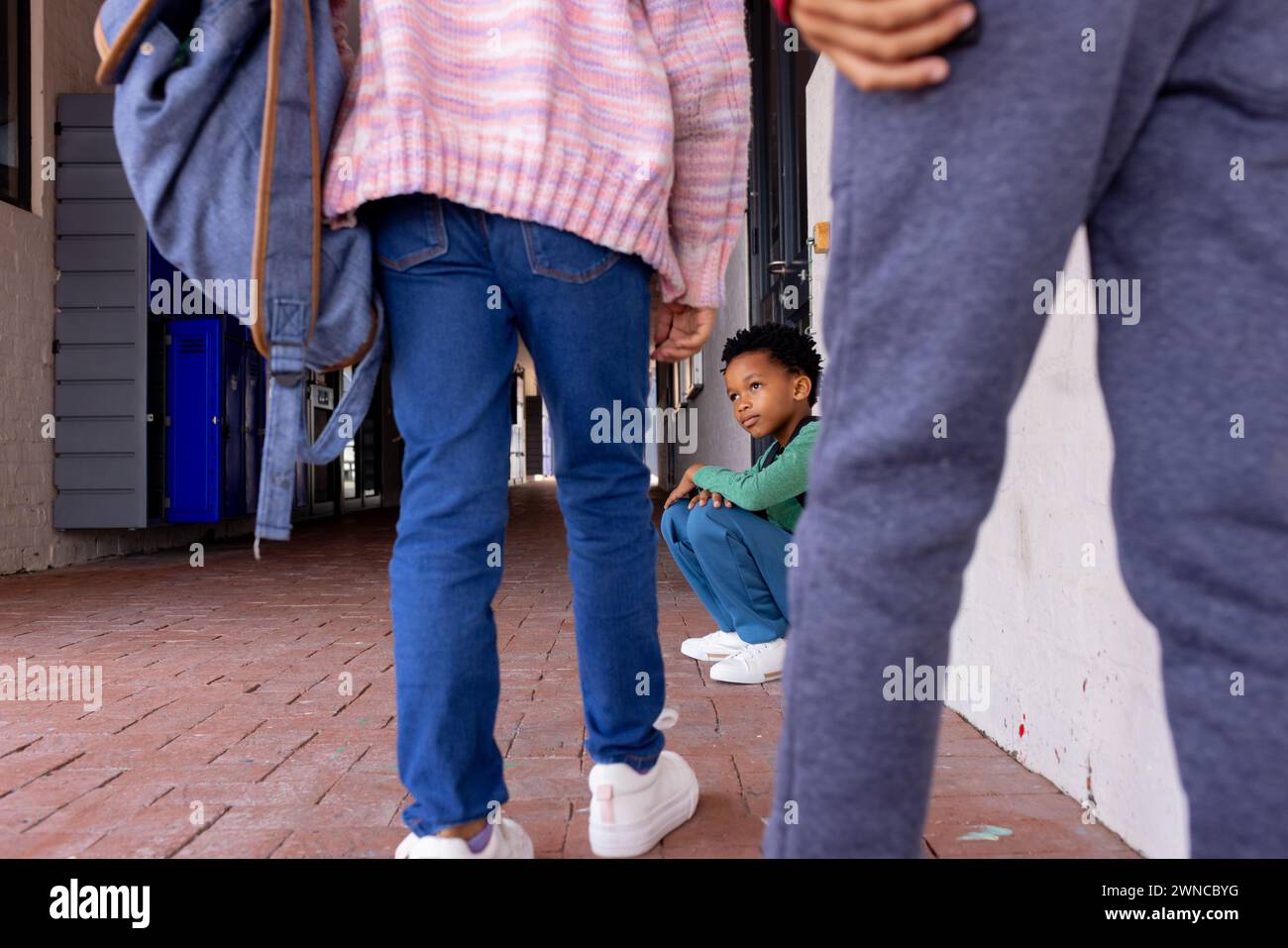 African American boy sits crouched between other children in school, looking sad Stock Photo