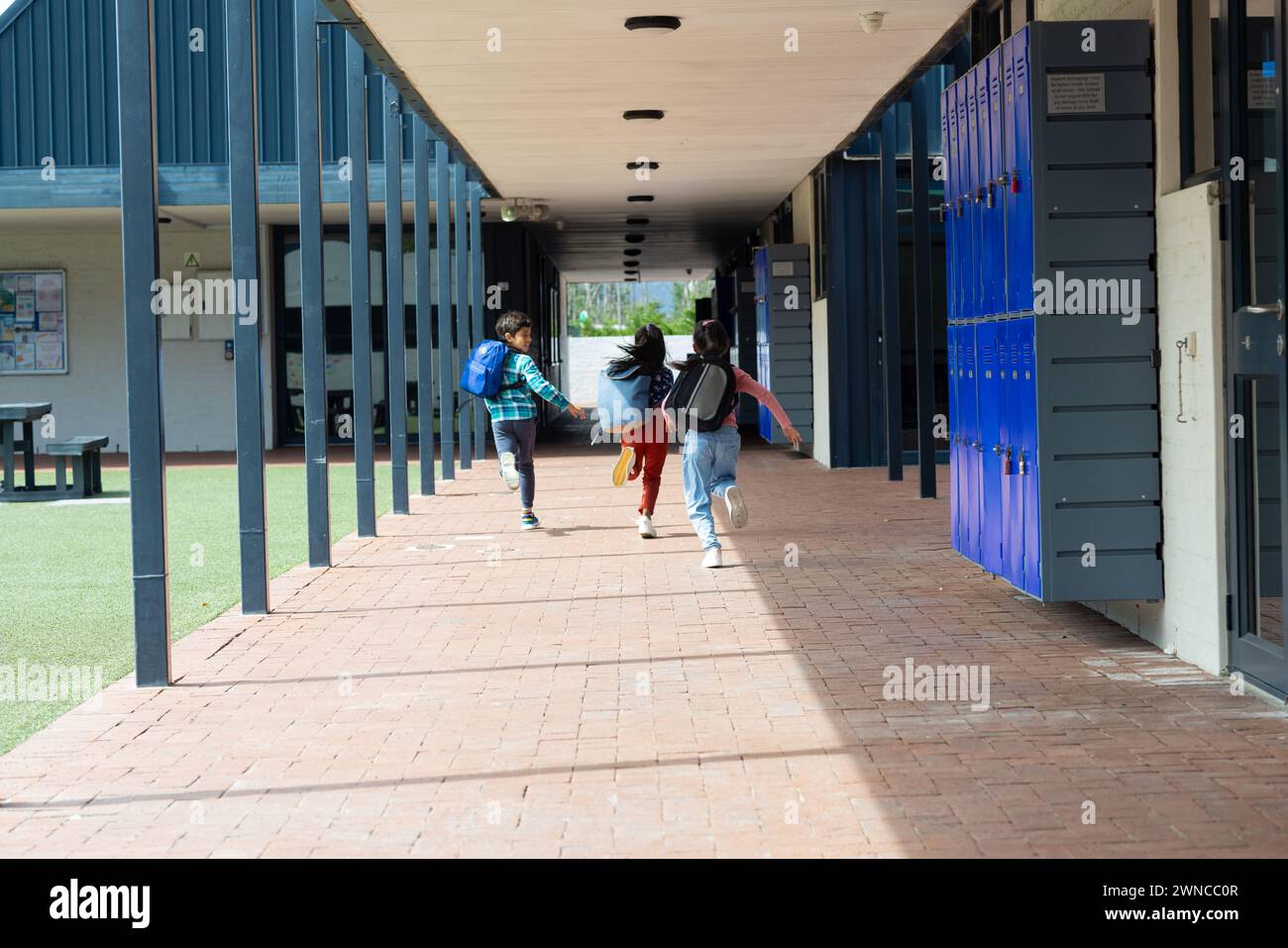 Three children are running through a school corridor with backpacks, with copy space Stock Photo