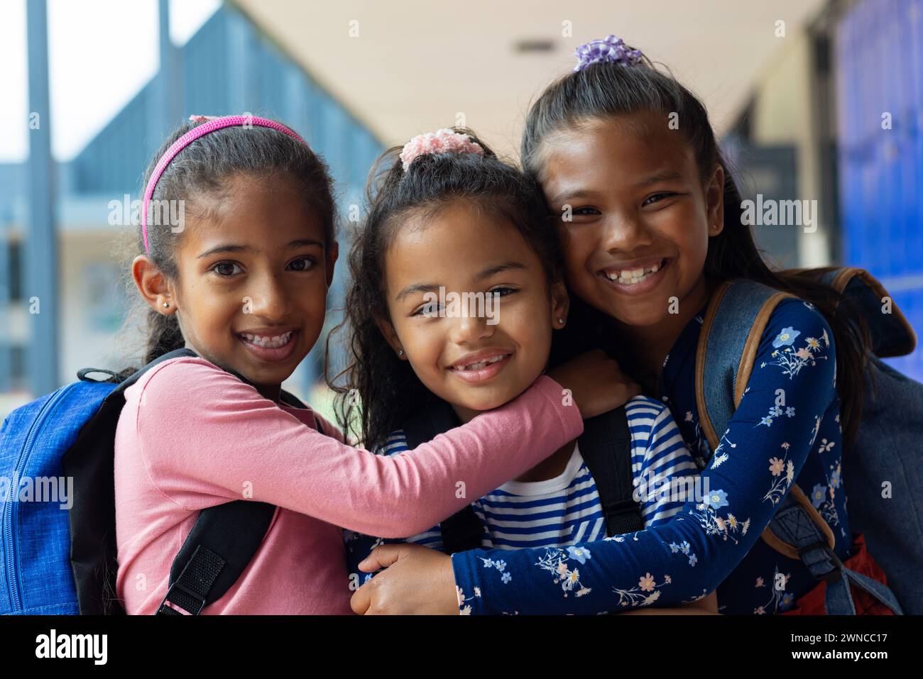 Three biracial girls are smiling and embracing in a school setting Stock Photo
