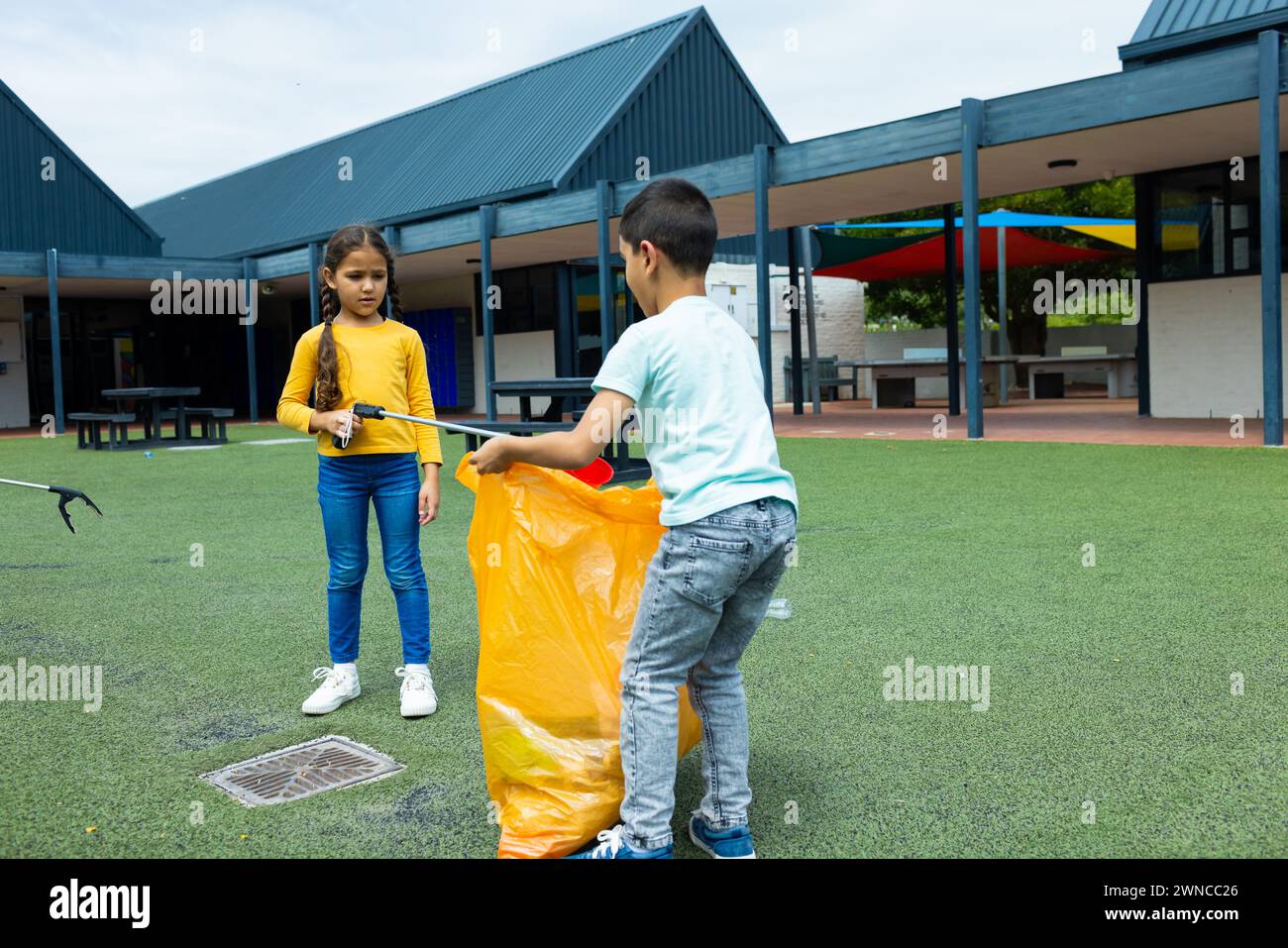 Biracial girl and boy are picking up trash, the girl in a yellow top and the boy in a white tee Stock Photo