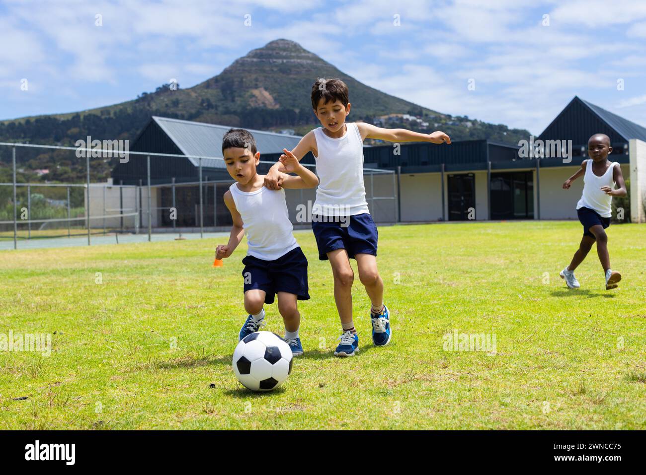 Biracial and African American boys play soccer outdoors at school, with ...