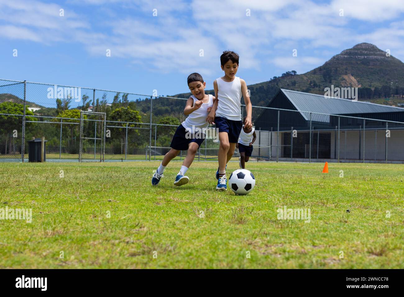 Two boys are playing soccer on a sunny day in school, with one chasing the ball Stock Photo