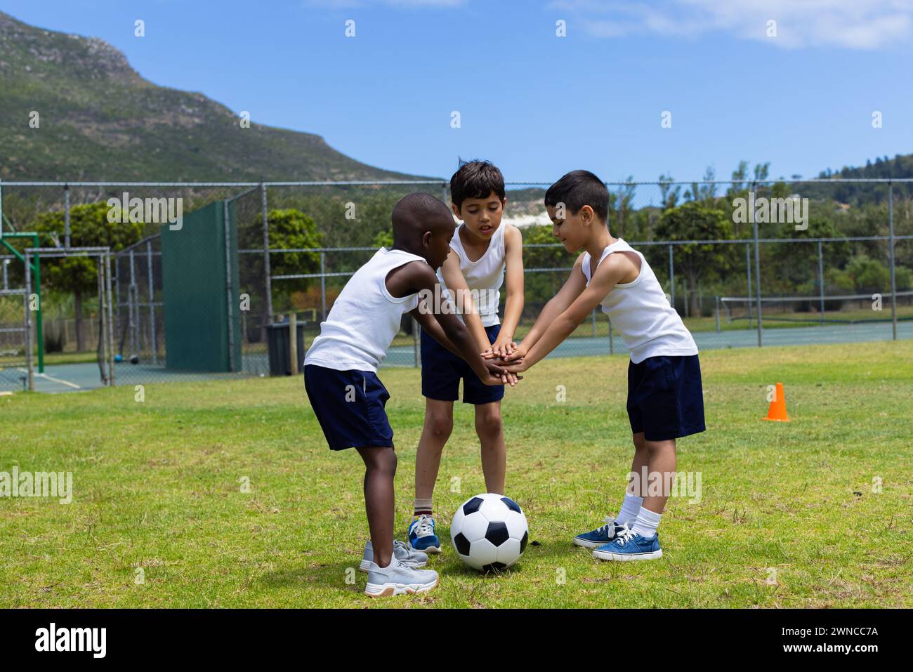 Three boys are huddled over a soccer ball on a grassy field, ready to play in school Stock Photo