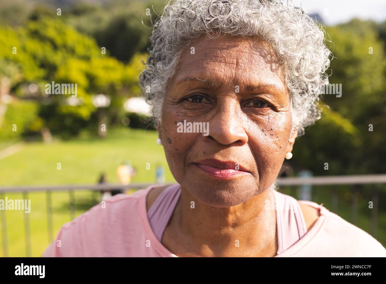 Senior biracial woman with grey hair and warm brown eyes stands outdoors Stock Photo