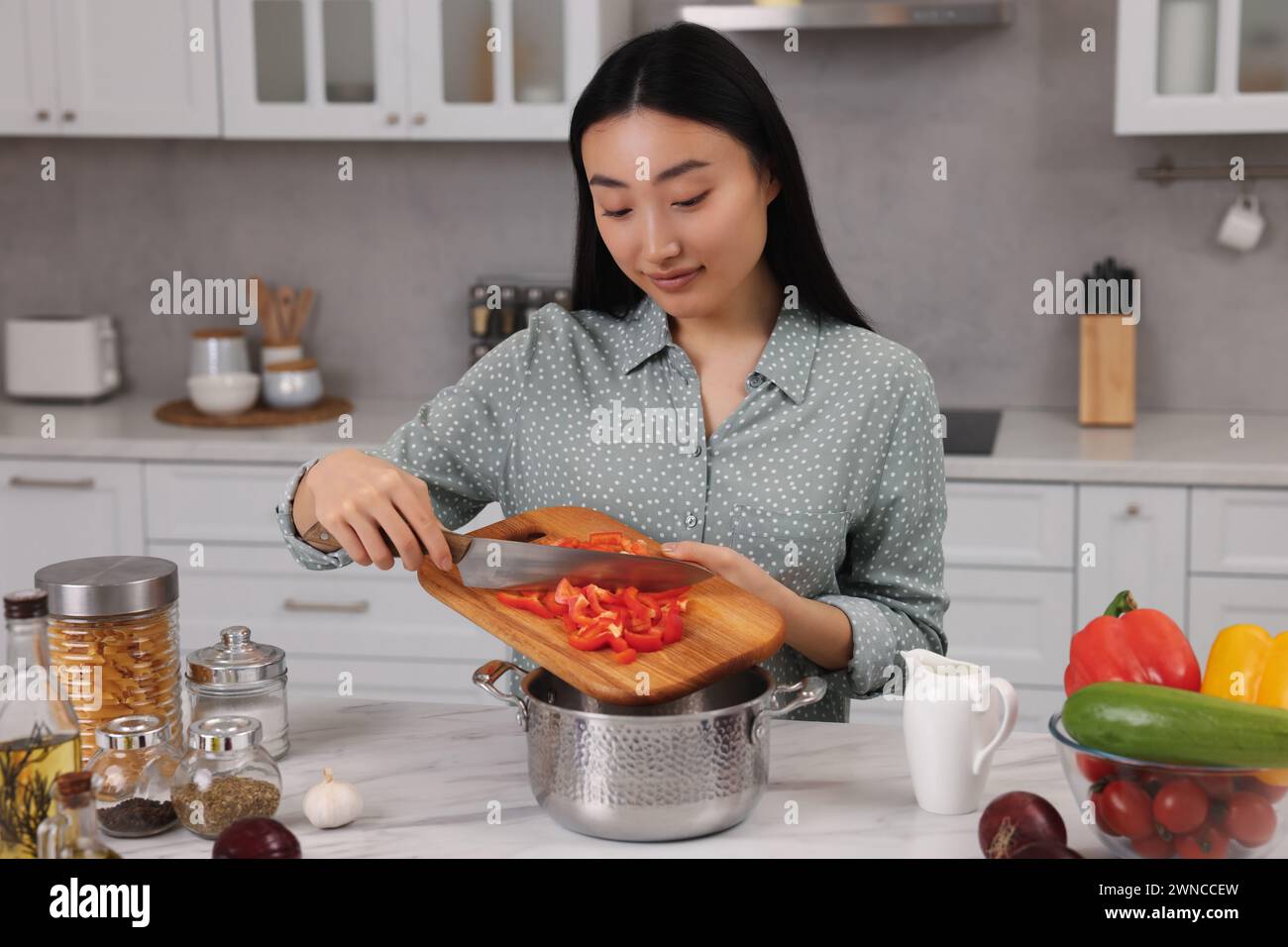 Cooking process. Beautiful woman adding cut bell pepper into pot in ...