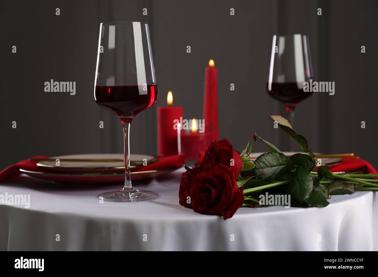 Place setting with roses and candles on white table. Romantic dinner ...