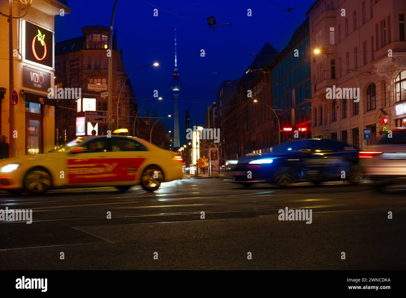 Cars driving down night Oranienburger street, Illuminated buildings and Fernsehturm TV tower visible in background, Nightlife, sustainability and envi Stock Photo