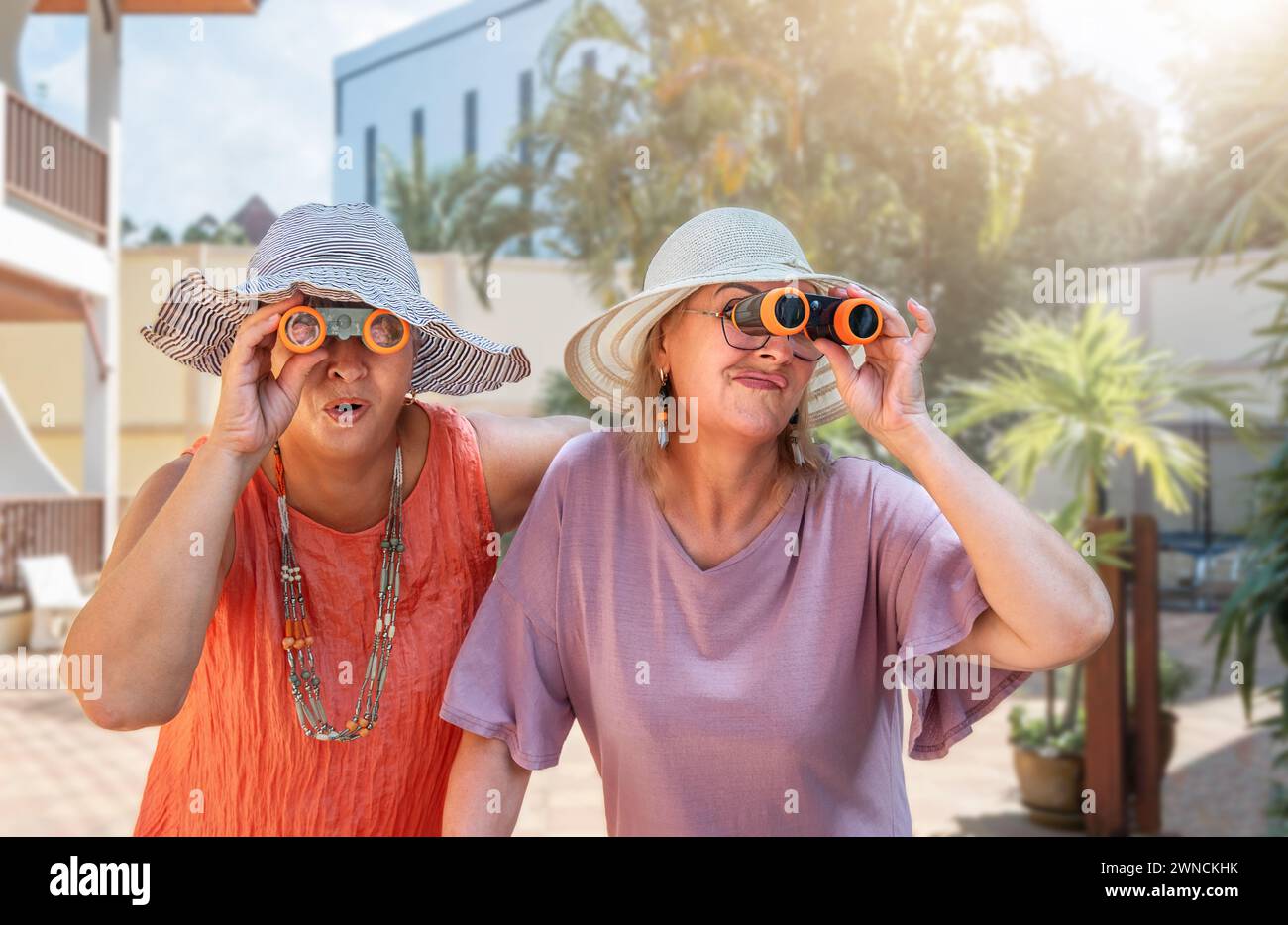 Senior girlfriends in hats and binoculars look in different directions at the resort Stock Photo