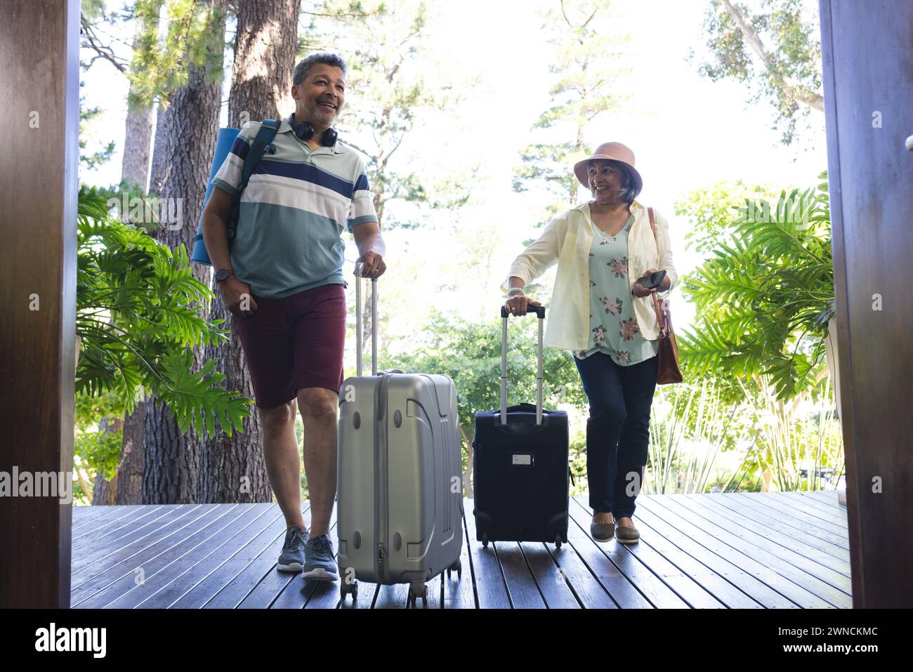 Senior biracial couple in casual vacation attire walking with suitcases Stock Photo