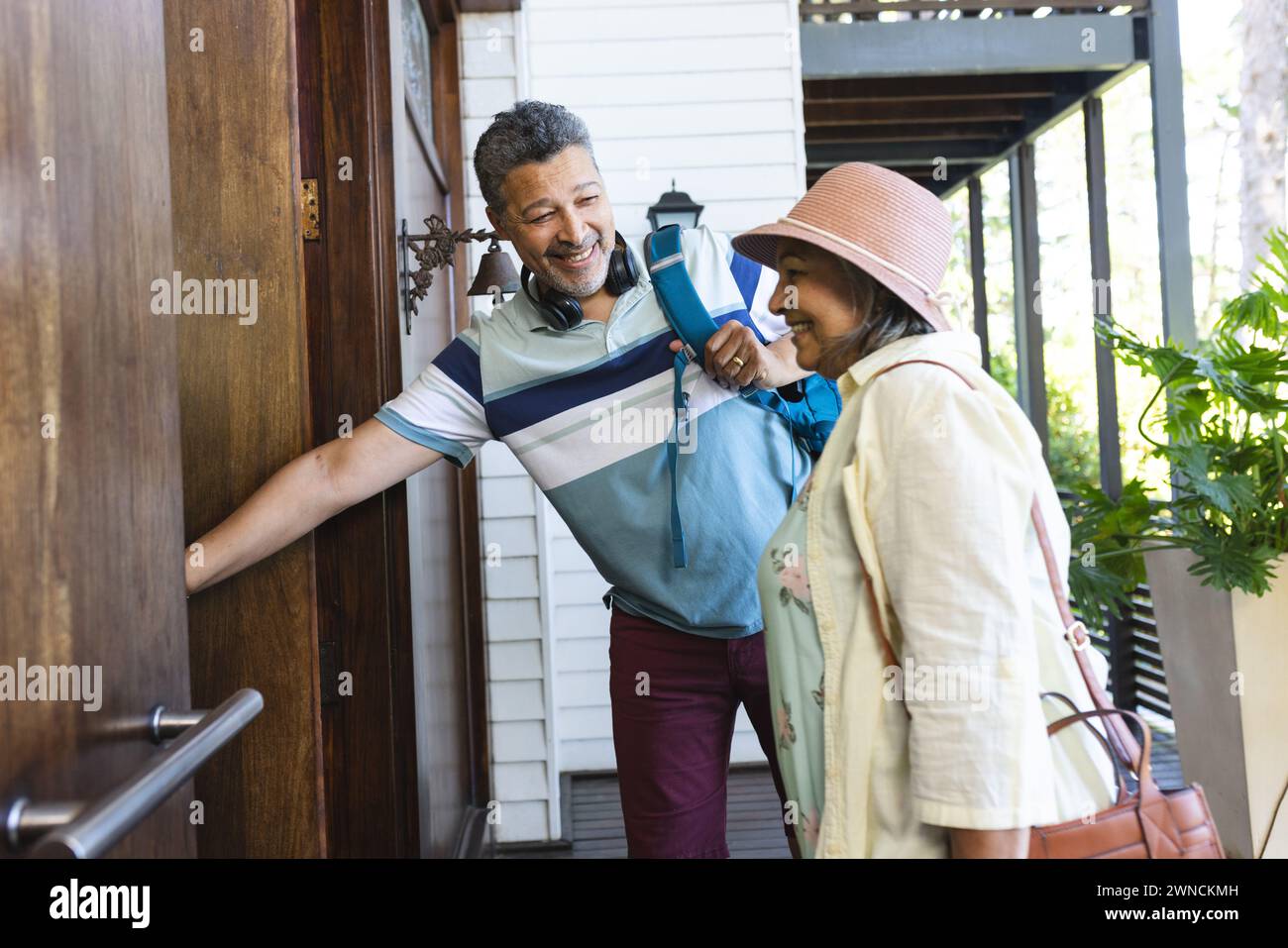 Senior biracial couple is smiling as the man opens a door for the woman Stock Photo