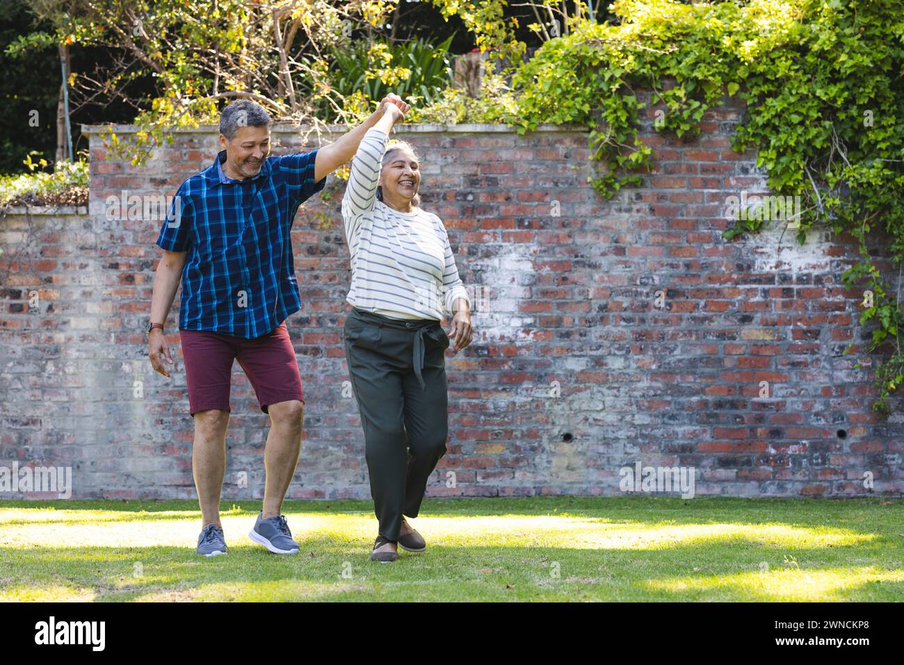 Senior biracial woman and man are dancing joyfully in a garden with copy space Stock Photo