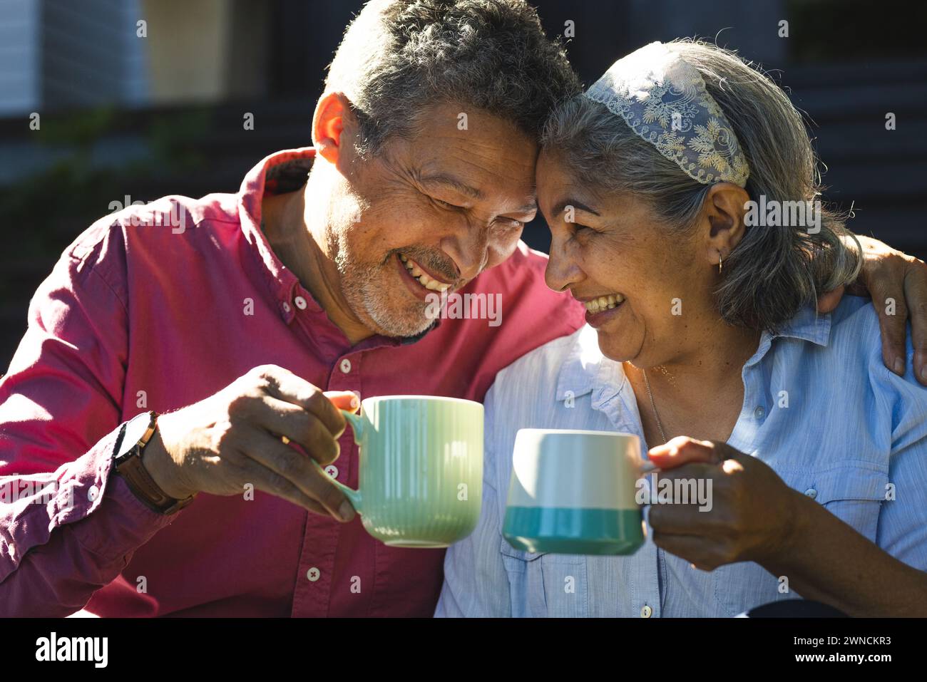 Senior biracial couple shares a joyful moment with a toast of coffee mugs Stock Photo