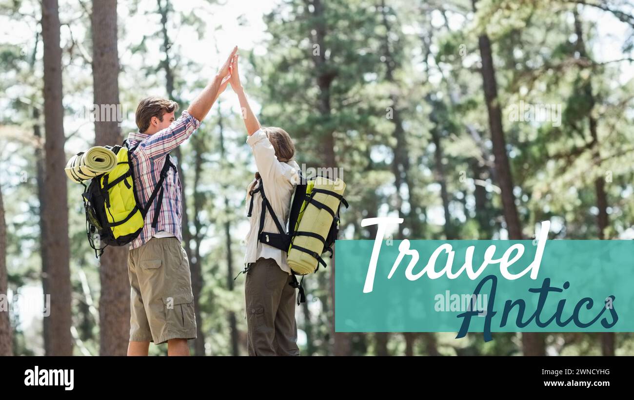 Travel antics text on blue band over caucasian couple wearing backpacks high fiving in forest Stock Photo