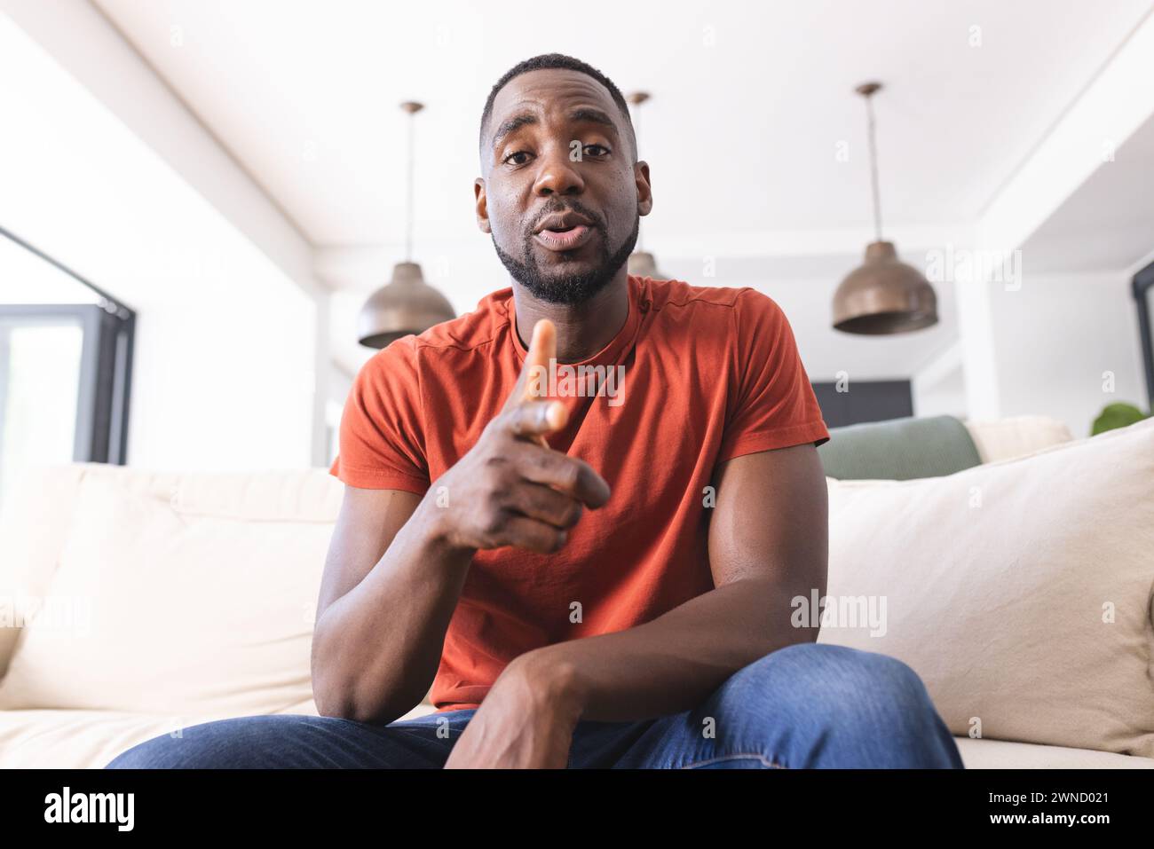 African American man in a red shirt is pointing towards the camera on a video call Stock Photo