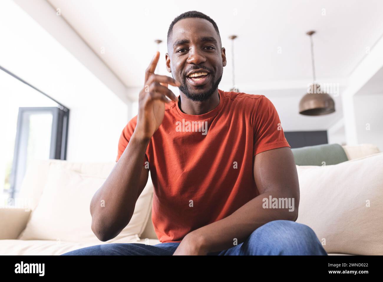 African American man in a red shirt gestures with his index finger, smiling warmly on a video call Stock Photo