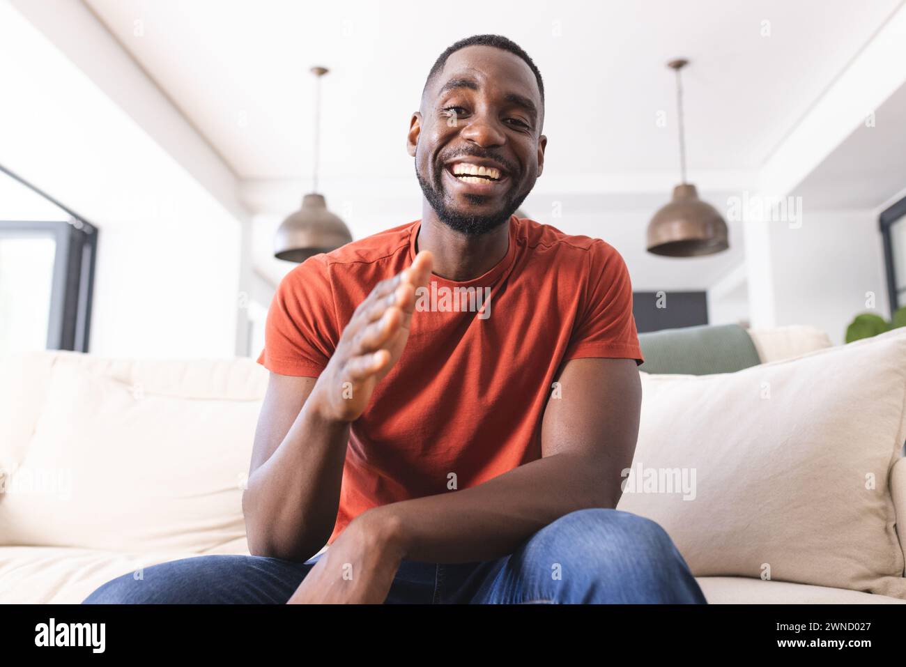 African American man in a red shirt is smiling and clapping on a video call Stock Photo