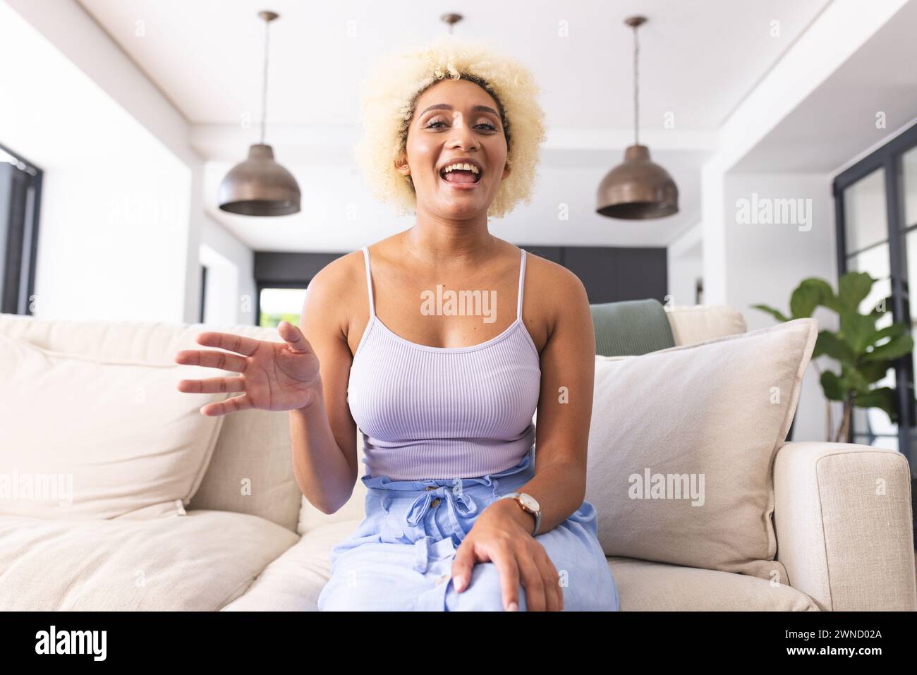 Young biracial woman with curly blonde hair smiles and gestures while ...