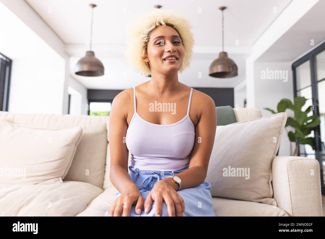 Young biracial woman with blonde curly hair sits comfortably on a beige ...