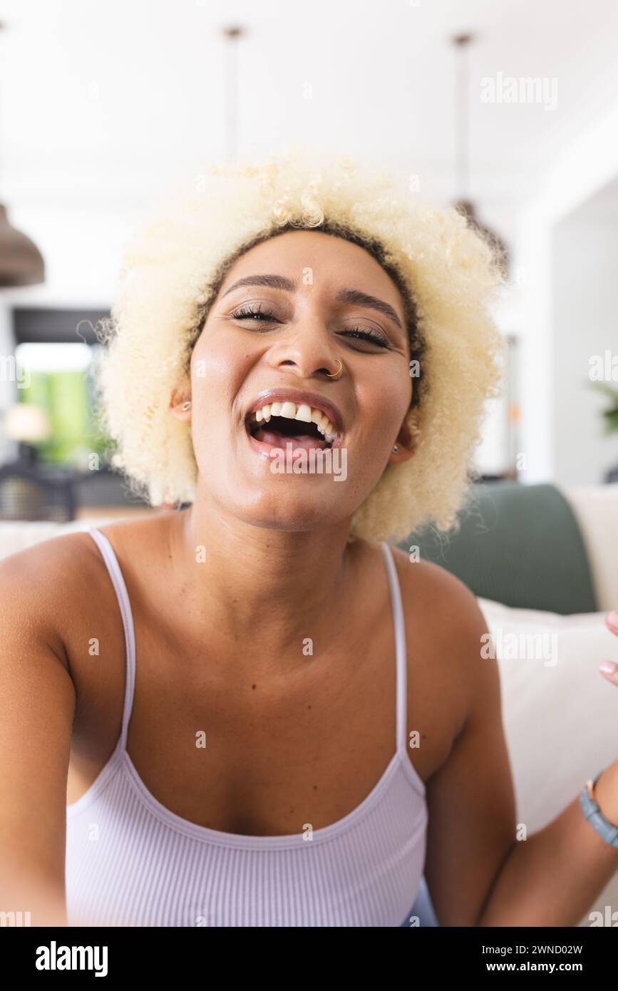 Young biracial woman with blonde hair laughs joyfully on video call, wearing a white tank top Stock Photo