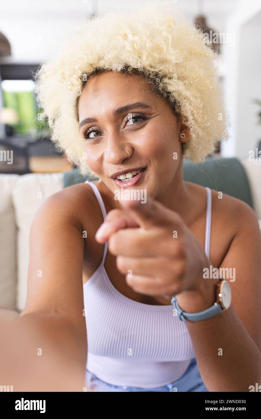 Young biracial woman with curly blonde hair is pointing and smiling at ...