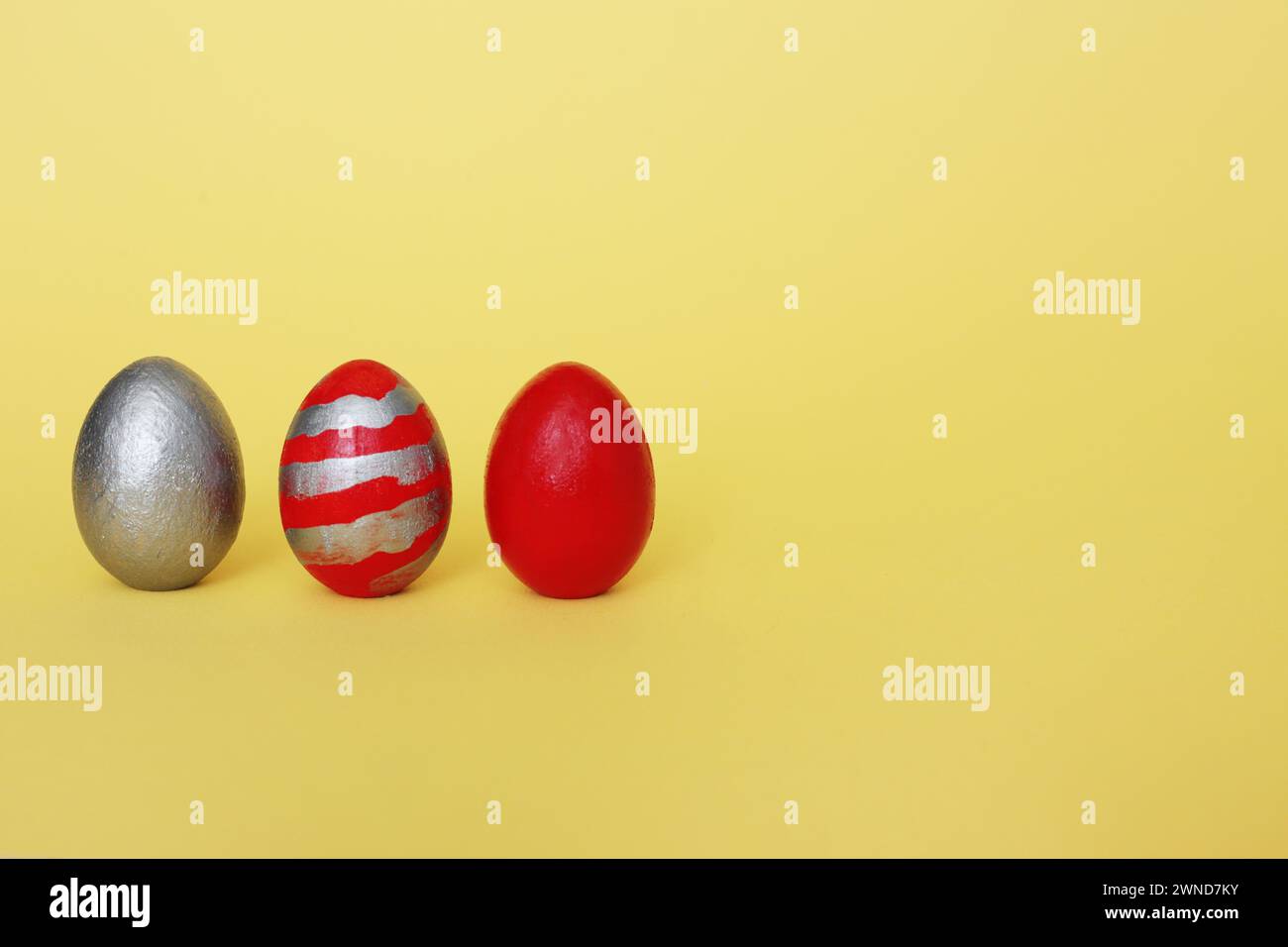 Three multi-colored decorative freshly painted eggs on a yellow background. Colored easter eggs on a light background Stock Photo