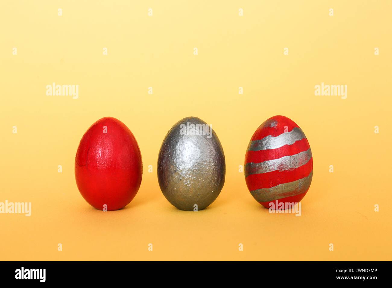 Three multi-colored decorative freshly painted eggs on a yellow background. Colored easter eggs on a light background Stock Photo