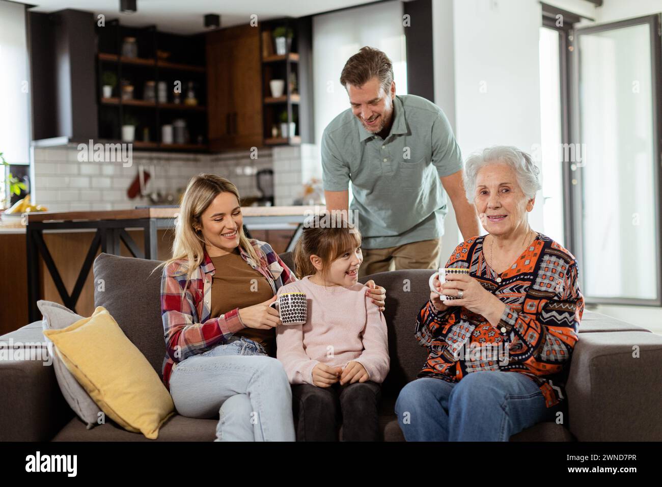 Heartwarming scene unfolds as a multi-generational family gathers on a couch to present a birthday cake to a delighted grandmother, creating memories Stock Photo