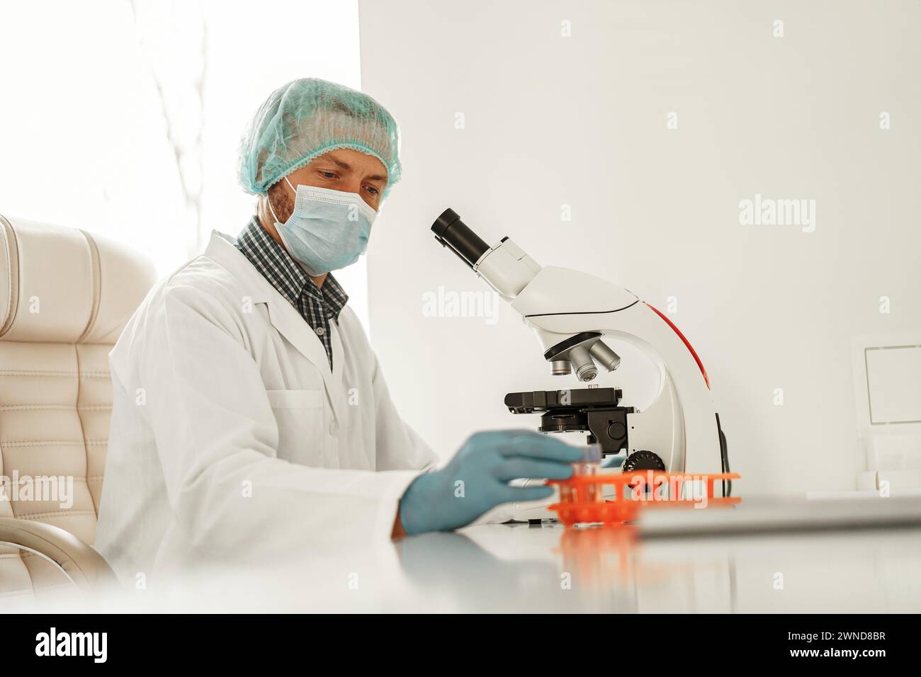 Male scientist looking under microscope does analysis of test sample in ...