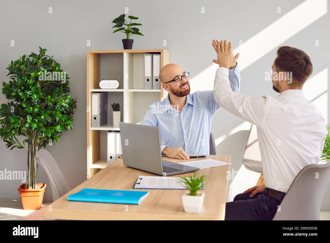 Two friendly male colleagues compliting task and giving high five Stock Photo