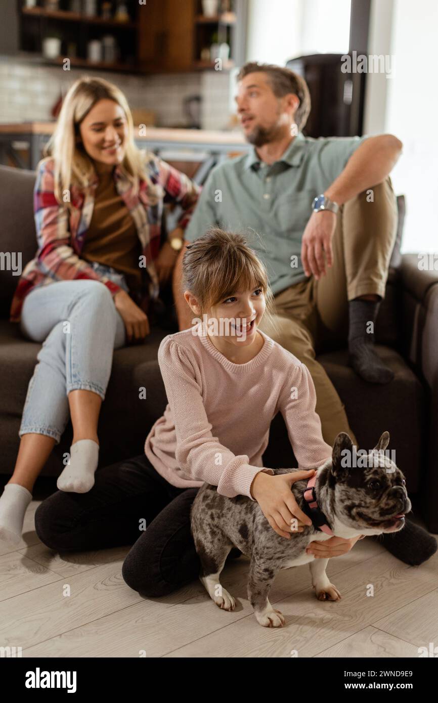 Joyful parents watch their daughter play with a happy french bulldog at home Stock Photo