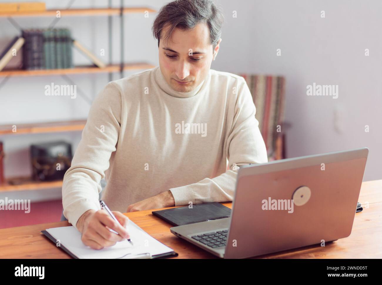 A graphic designer in the office works at a laptop and graphics tablet, sketching with a pencil on paper. Focus on a concentrated face. Stock Photo