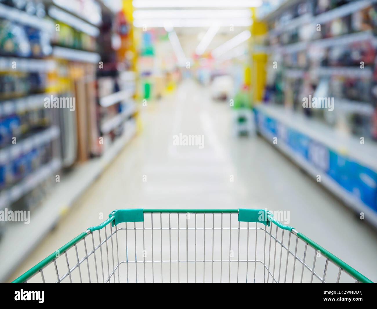 Supermarket aisle with empty green shopping cart blurred background ...