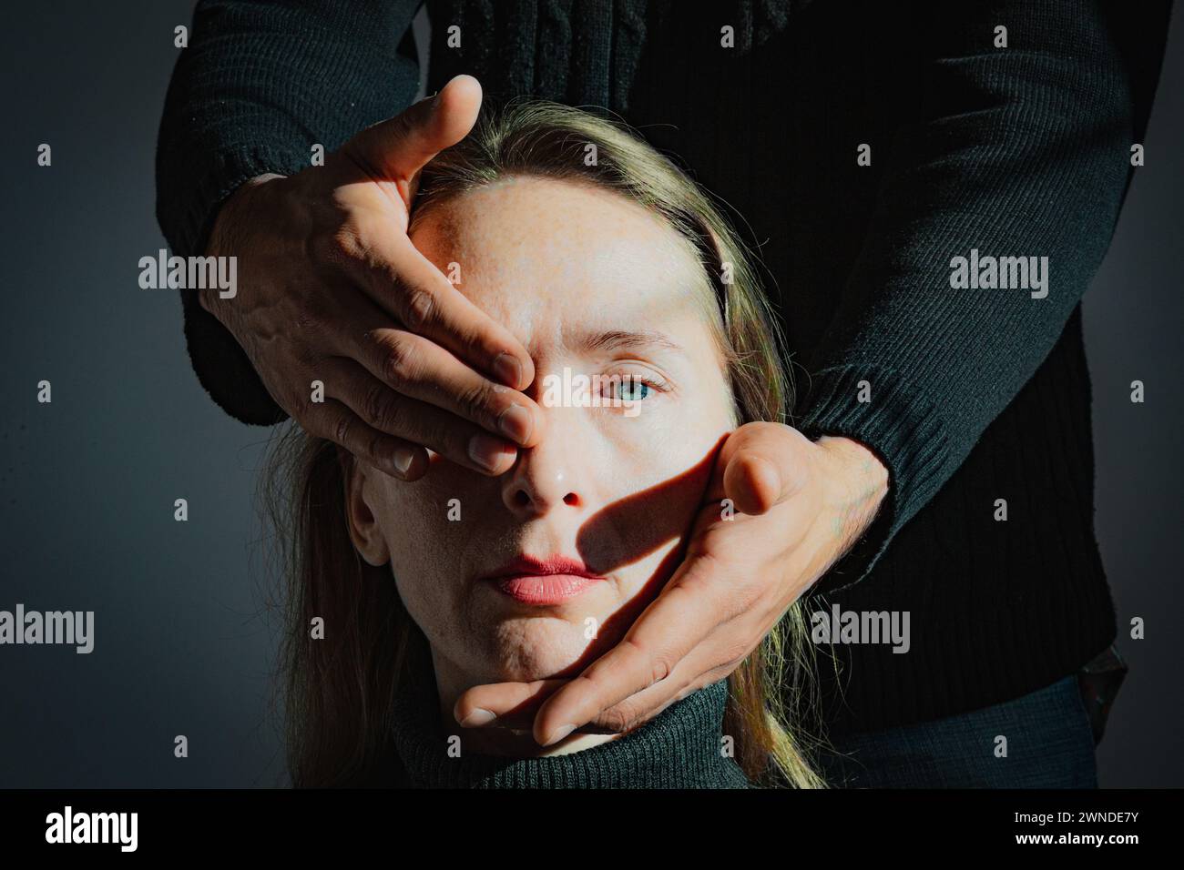 Visualization of a psychological problem. Difficulties in mutual understanding. A man holds the head of an adult young woman in his hands, closing one Stock Photo