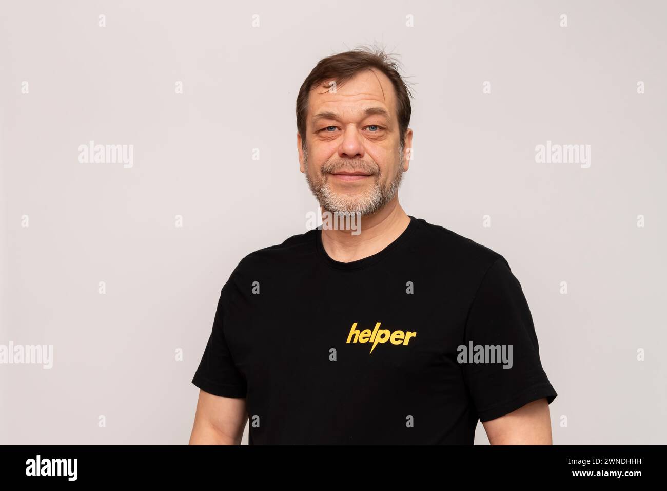 Elderly man 50-55 years old wearing a black T-shirt that says: Helper. Looking into the camera on a white background. Stock Photo