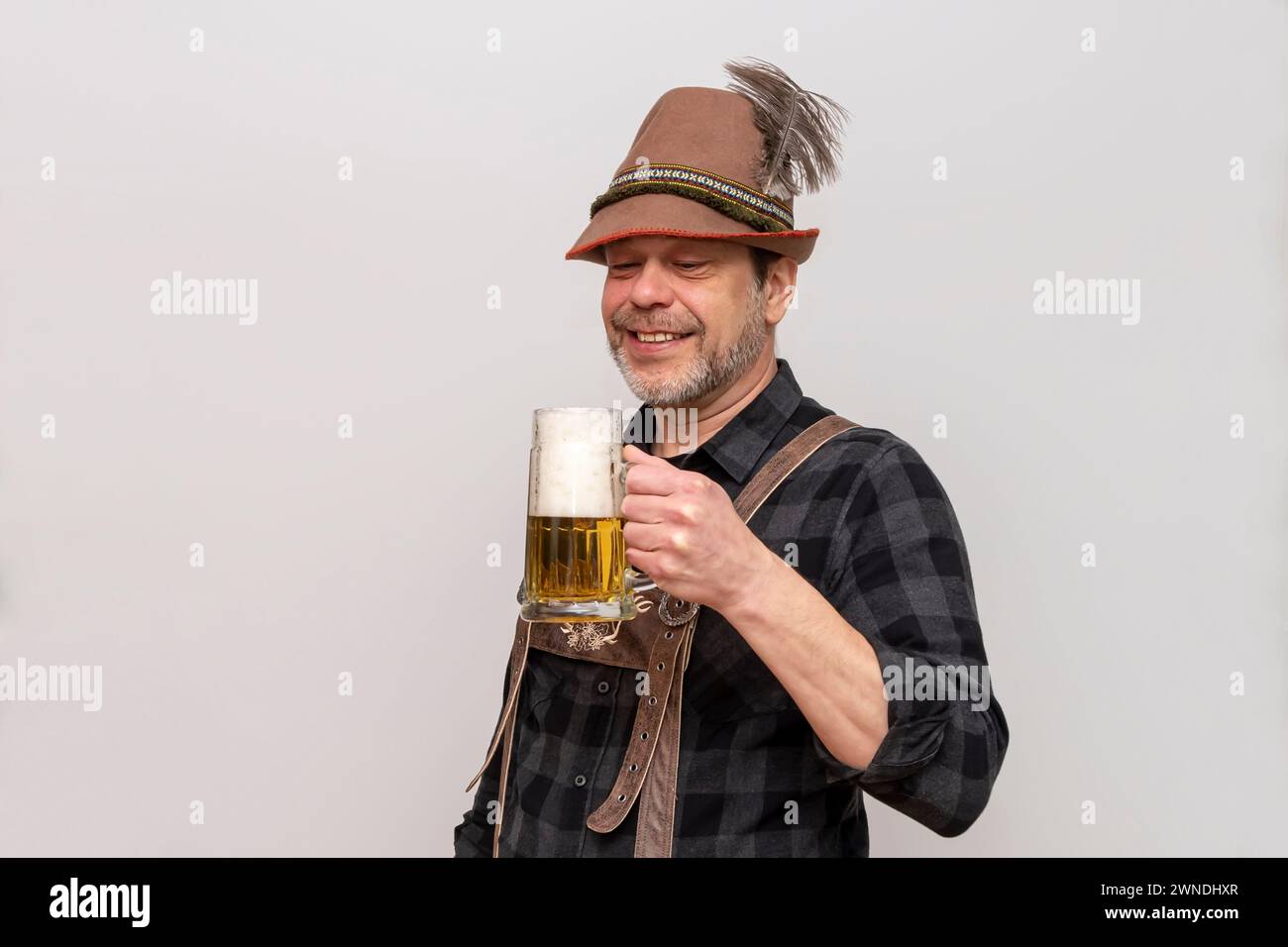Elderly bearded man in hat wants to drink a glass of beer with foam, beer festival in Austria and Germany. Stock Photo
