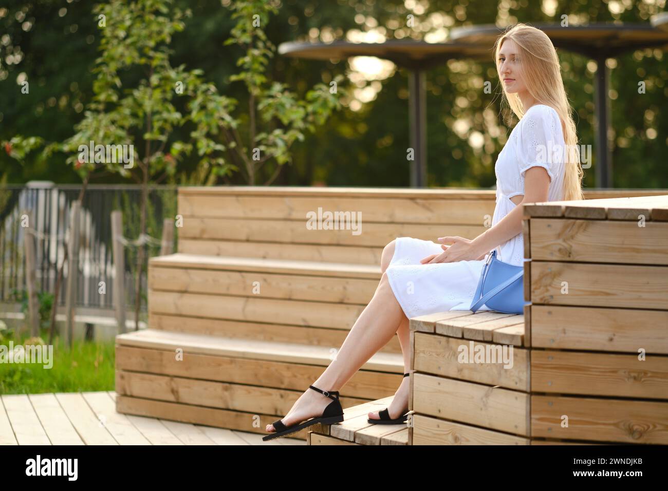 Young woman in white dress sitting on bench Stock Photo - Alamy